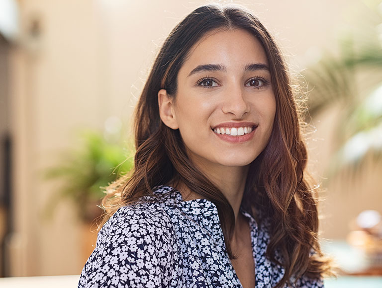 Smiling woman with healthy teeth, showcasing aesthetic results of porcelain implant bridges in a dental practice setting.