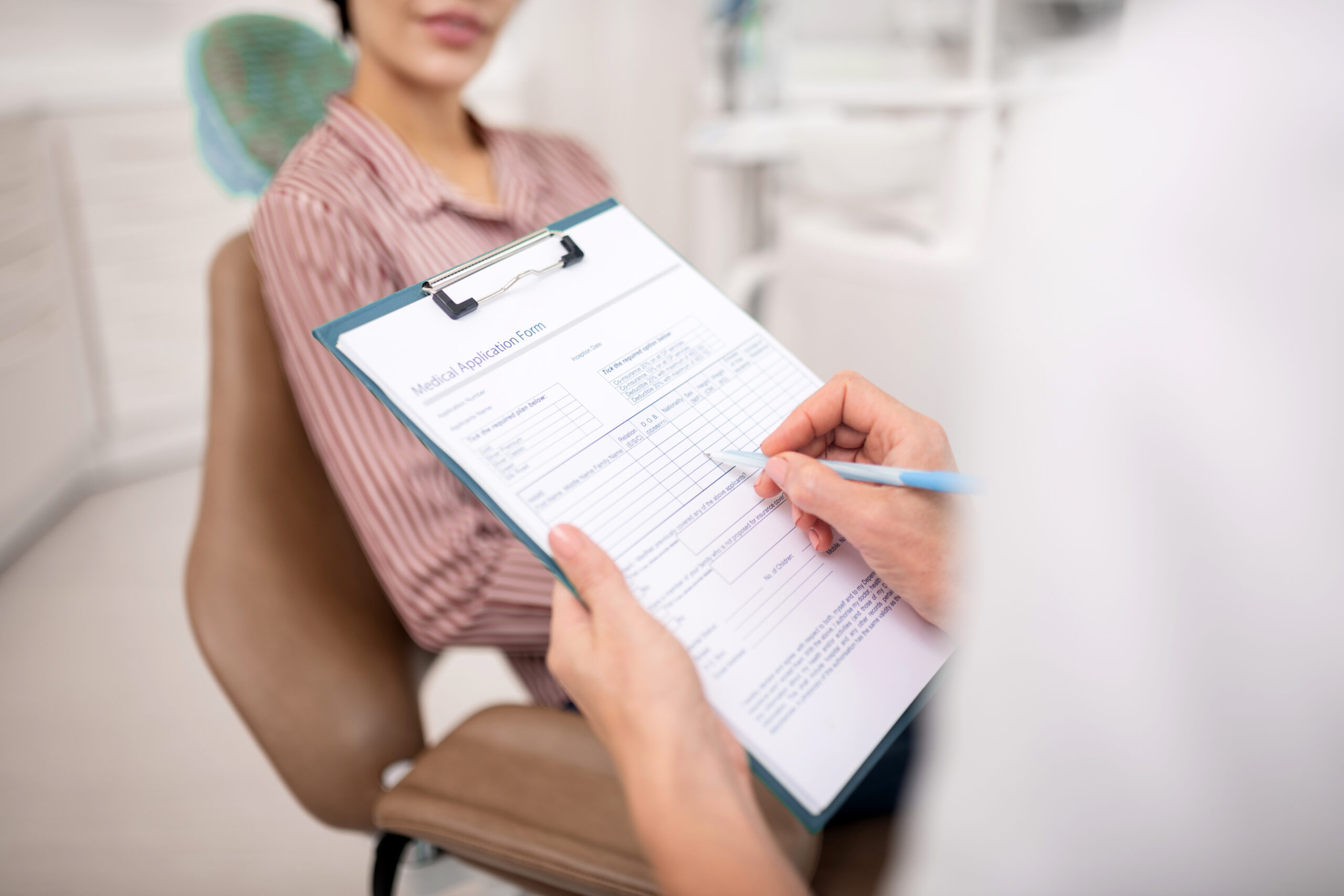 Patient filling out a medical application form in a dental office, preparing for bone grafting consultation for dental implants.