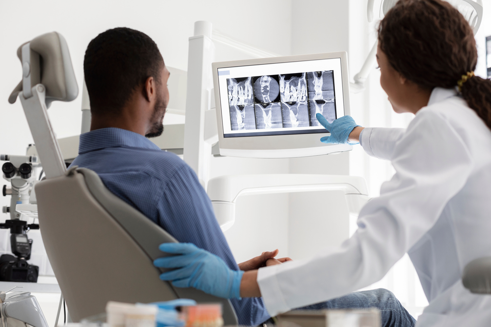 Patient in dental chair reviewing X-ray images with dentist, discussing bone grafting options for dental implants.