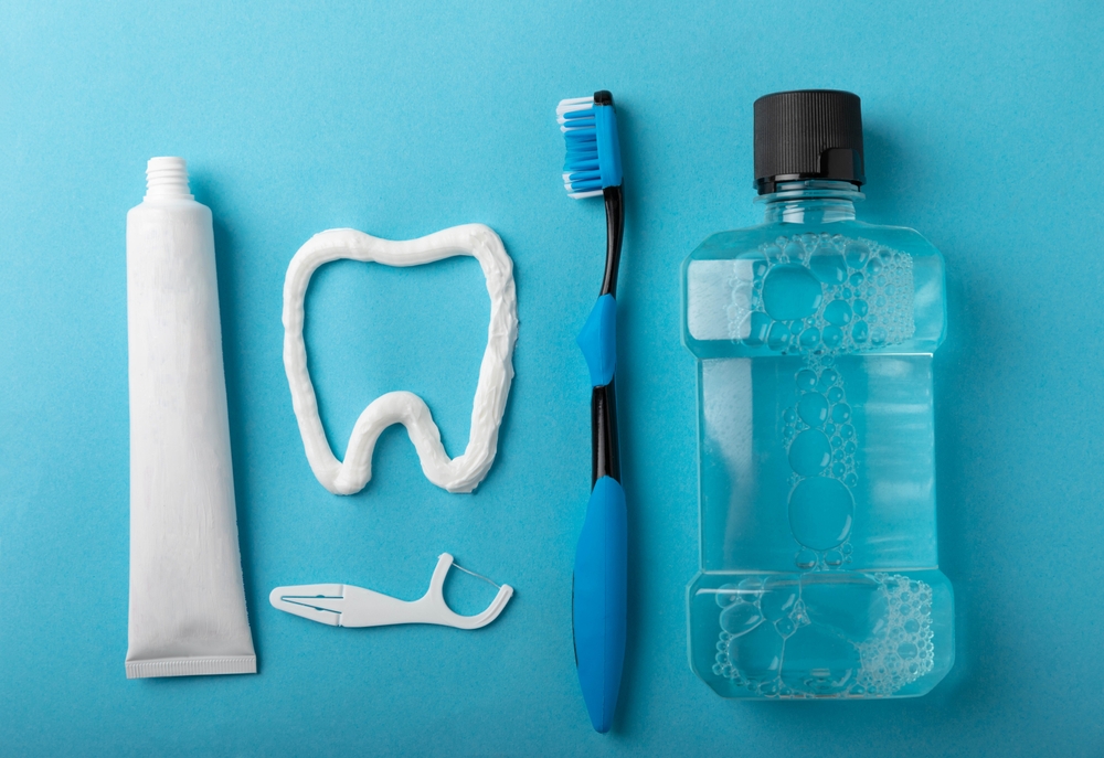Dental care essentials including toothpaste, a toothbrush, dental floss, and mouthwash on a blue background, emphasizing daily oral hygiene for dental implant maintenance.